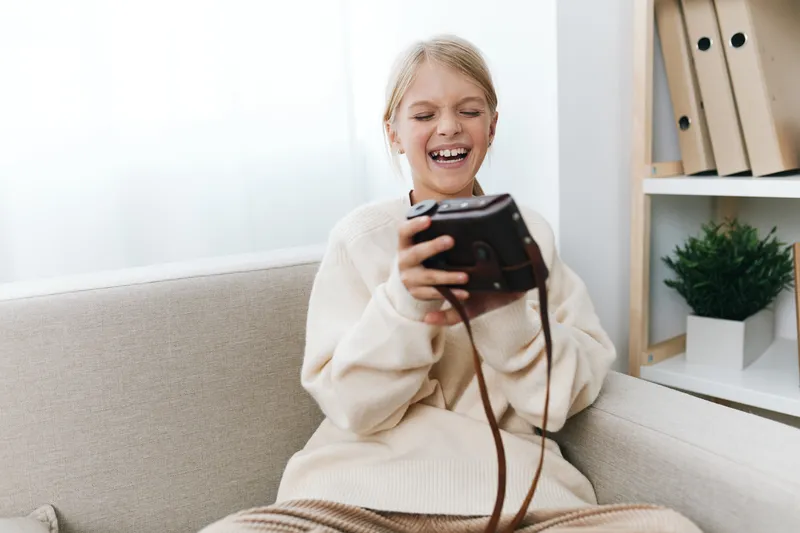 Authentic lifestyle scene shows a cheerful student at home enjoying a handheld game device, blending school routines with play in a cozy, sunlit living room.