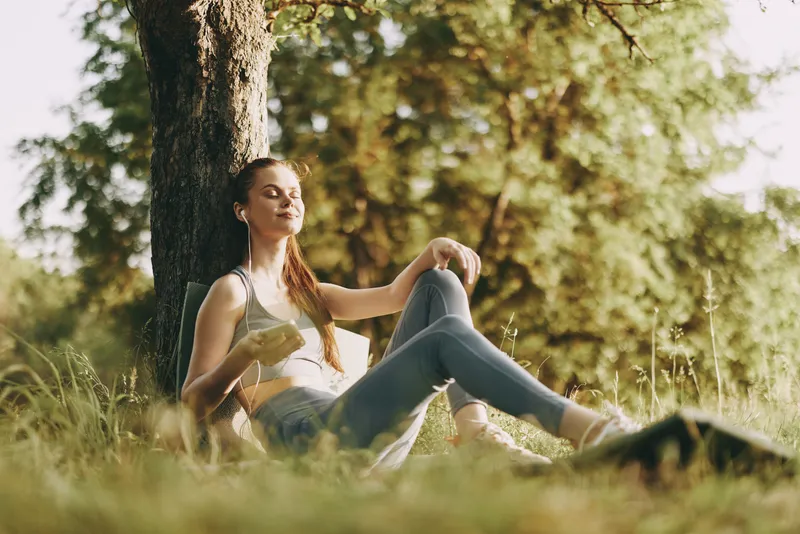 Young woman enjoying a healthy snack outdoors in a sunlit park, surrounded by greenery, conveying a sense of relaxation and well being in a seasonal setting