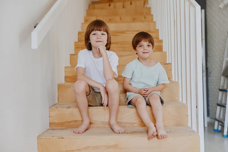 Two smiling boys happily sitting on wooden stairs, showcasing warmth and friendship in a bright, modern home setting filled with natural light.