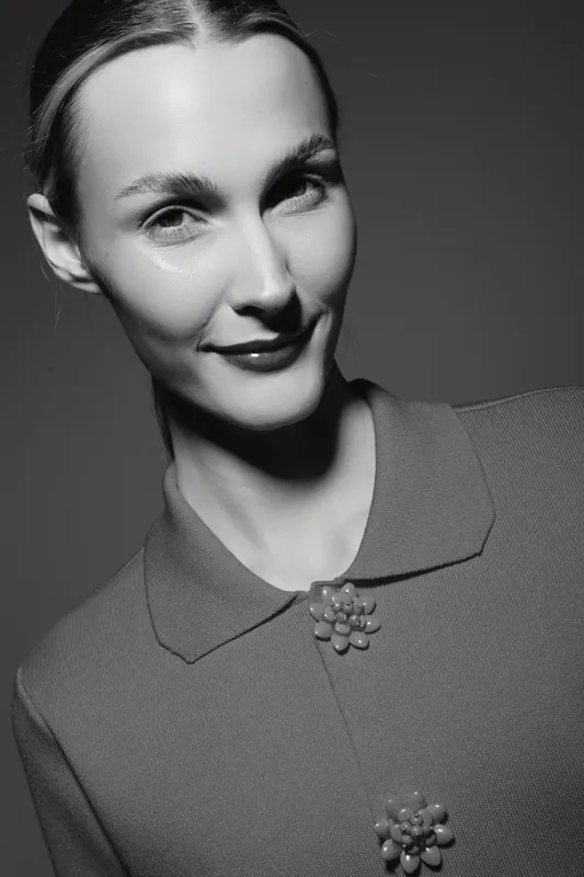 Portrait of a young white woman with light skin and slicked-back hair wearing a textured top with decorative buttons in black and white.