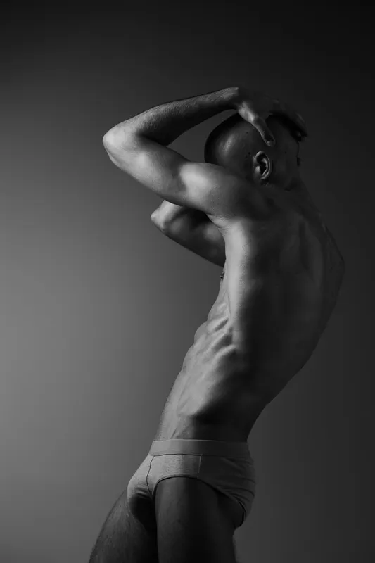 Black and white image of a man striking a dynamic pose showcasing strength, grace, and athleticism, highlighting the beauty of the human form through contrasts.