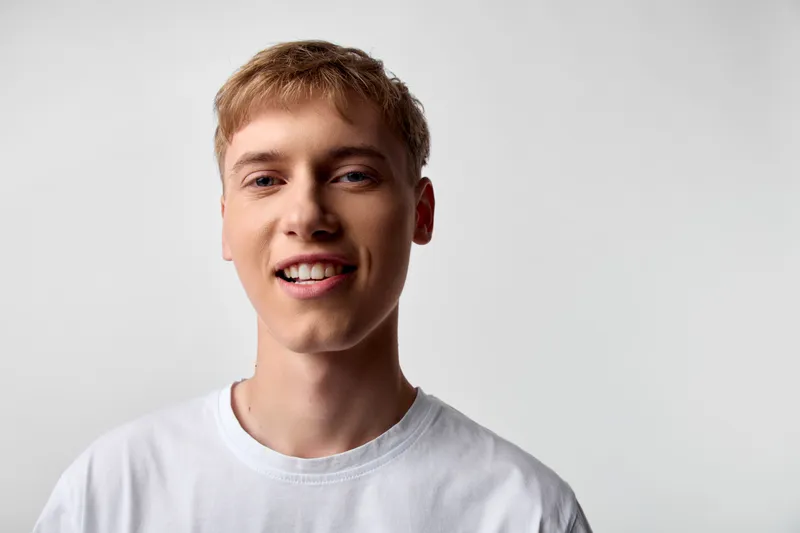 Young man smiling in a white t shirt, casual wear in a studio with a neutral background, headshot style, clear lighting and minimal composition for stock use