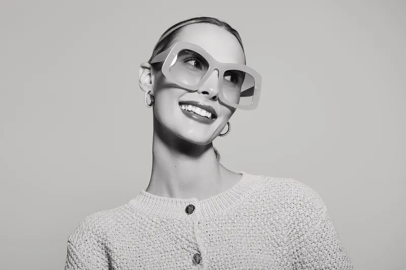 Smiling white woman with pale skin wearing large sunglasses and knitted sweater looks sideways in studio. Concept for fashion, style, and confident female portrait.