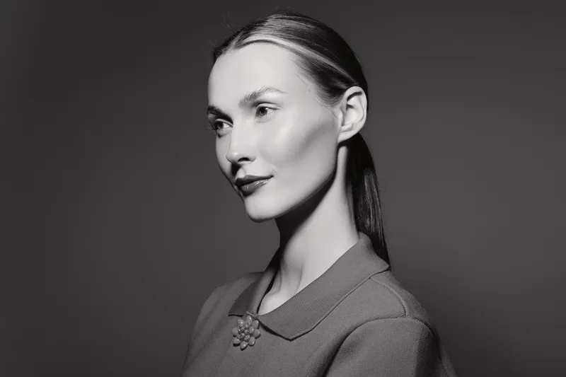 Portrait of a white woman with pale skin and dark hair in black and white. Studio lighting highlights facial features and classic style.