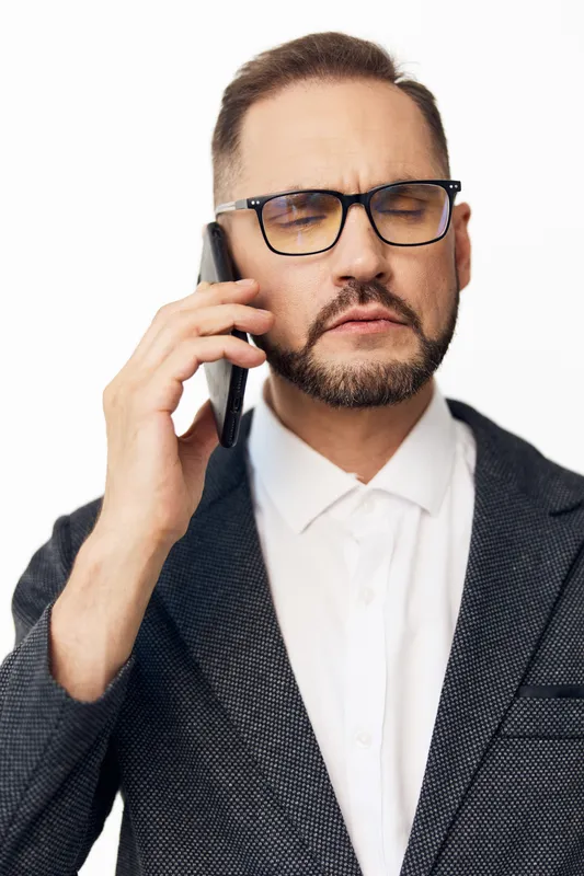A focused business professional man speaks on a mobile phone against a clean white background, conveying concentration, seriousness, and a confident mindset.