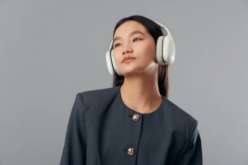 Young woman with headphones and dark blazer posing on gray background with contemplative expression looking aside. Fashion, technology and casual style with confident attitude in studio.