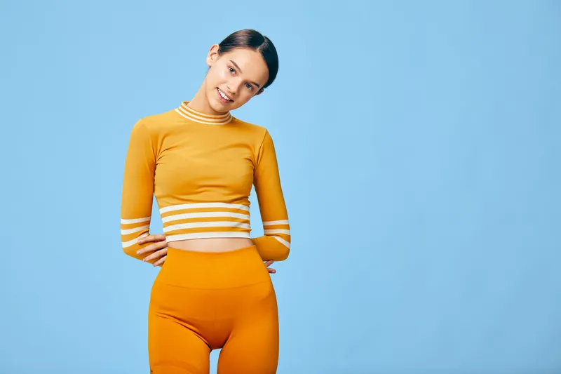Female fitness model wearing orange workout set posing in a studio with a blue background, showcasing athleticwear, confidence and healthy lifestyle for sport and active living.
