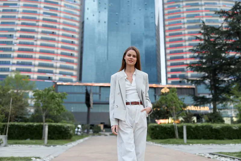 business woman standing confidently in modern cityscape wearing stylish white suit with blue glass skyscrapers and green park background
