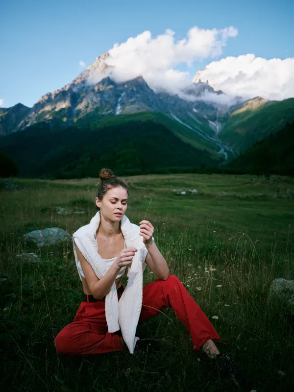 Woman rests in a meadow among mountains, a calm nature moment outdoors, capturing relaxation in alpine landscape with rolling hills and dramatic peaks under a bright sky