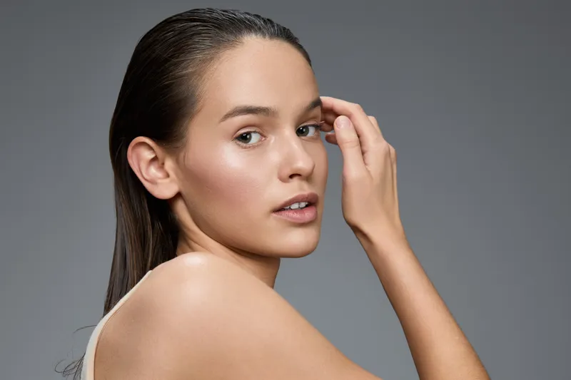 Portrait of a young woman with long hair, showcasing natural beauty and a serene expression against a soft gray background, emphasizing health and self care