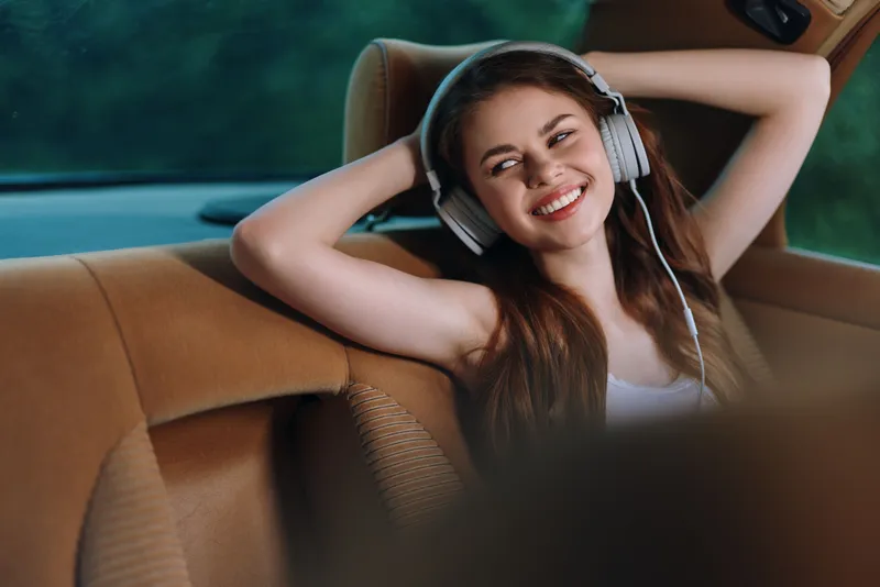 Young woman enjoying music in a car with headphones, smiling joyfully against a soft green background. Perfect for capturing the essence of relaxation and happiness.