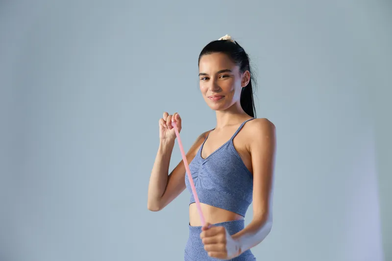 Sport fitness woman exercising with resistance band, wearing blue workout clothes, smiling, healthy lifestyle, active young female training indoors.