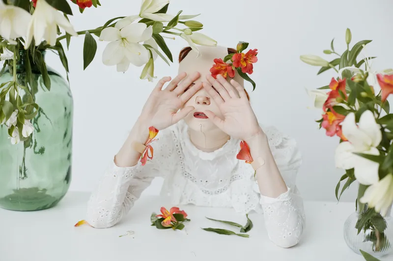 Young woman with flowers covering her face, expressing serenity and introspection in a soft and bright atmosphere, ideal for themes of nature, beauty, and emotions