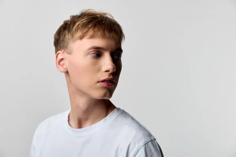 Man in a white t shirt posed against a light backdrop, turned to the side with a contemplative look, minimal studio style and clean casual fashion