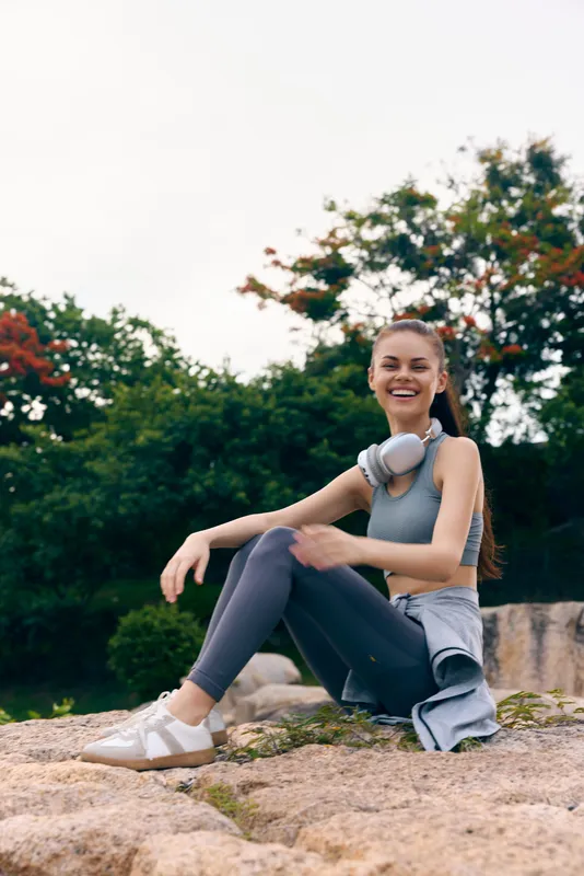Young woman in athletic wear, smiling joyfully outdoors, enjoying nature in a green park, conveying fitness and wellness concepts