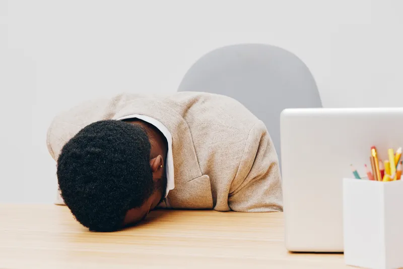 Overwhelmed stressed african american man in beige suit head down on desk frustrated tired exhausted concept workplace office environment