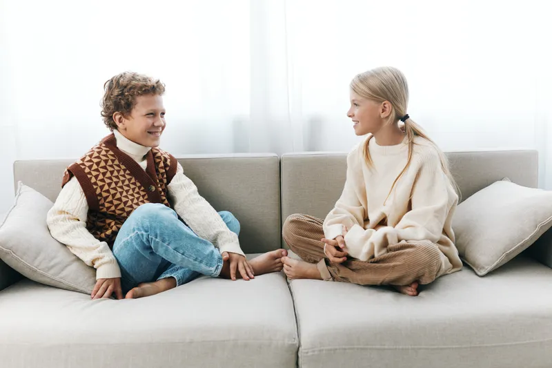 A candid, authentic moment of children at home on a cozy sofa, capturing a playful lifestyle and school inspired outfits in soft light.