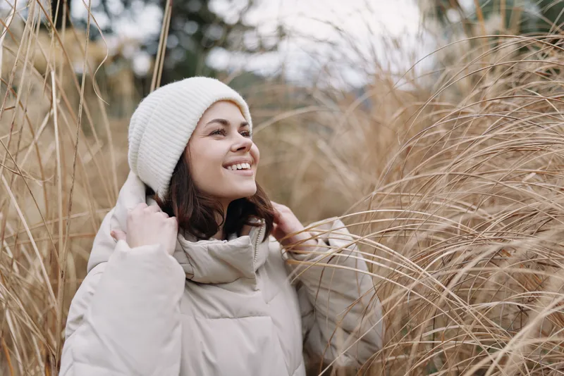 Woman, outdoor, coat, winter, smiling, fashion, portrait, nature, grass, calm in a field wearing a warm padded coat and beanie, enjoying serene daylight