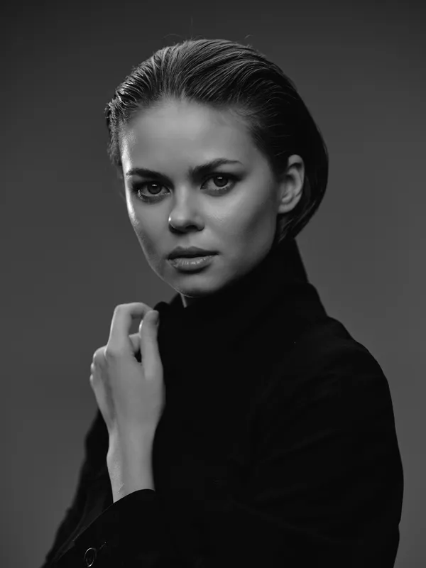 Black and white portrait of a serious woman in a black turtleneck with intense gaze and elegant pose in studio lighting.