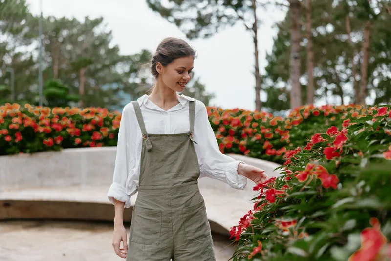 Young woman in casual attire enjoying flowers in a vibrant garden, expressing joy and serenity, perfect for seasonal and lifestyle themes