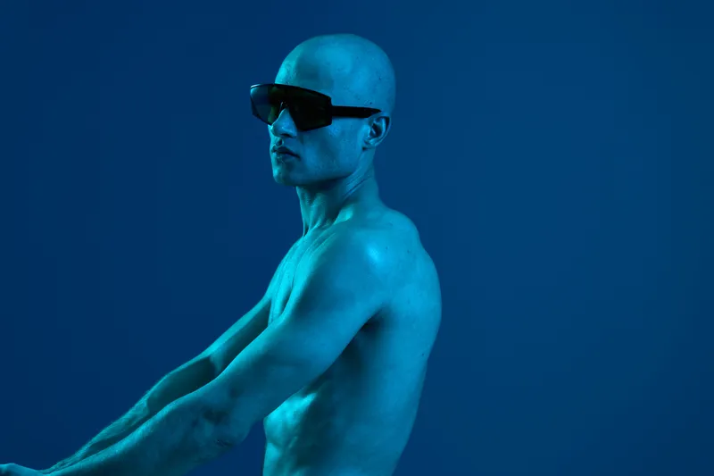 Confident man in sunglasses poses against a blue background. The image captures a striking black and white contrast, emphasizing strength and style.