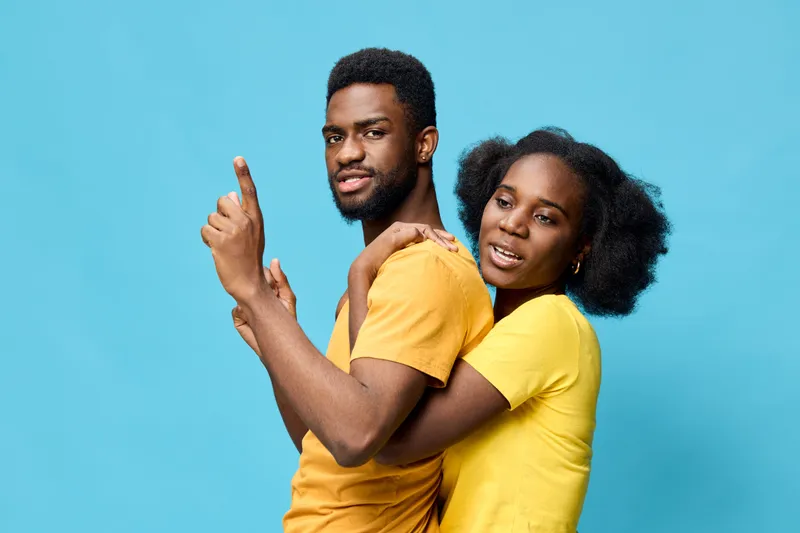 Young black couple in matching yellow shirts, joyfully posing against a bright blue background, expressing love and happiness in a vibrant and playful manner