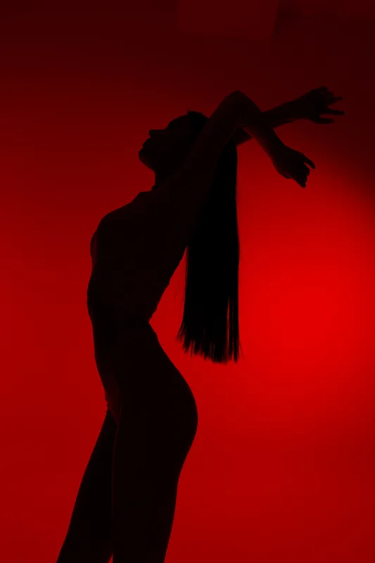 Silhouette of a woman sport fitness stretching with long hair against vivid red background, highlighting flexibility and strength in dynamic pose.