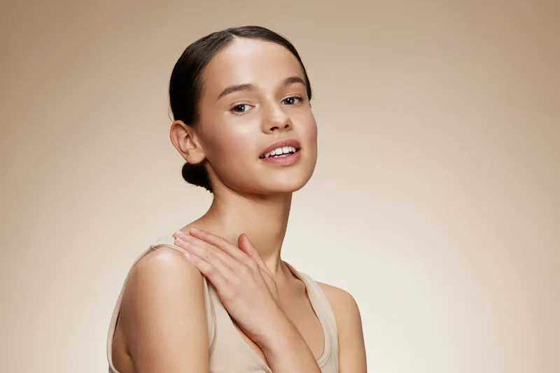 Beautiful young woman with a natural makeup look, softly lit against a beige backdrop, exuding confidence and grace, ideal for health and beauty concepts
