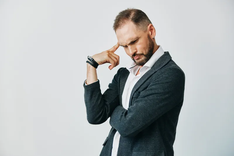A professional man in a suit stands against an isolated colored background, embodying business focus and calm, reflective emotion through his thoughtful stance and composed gaze.
