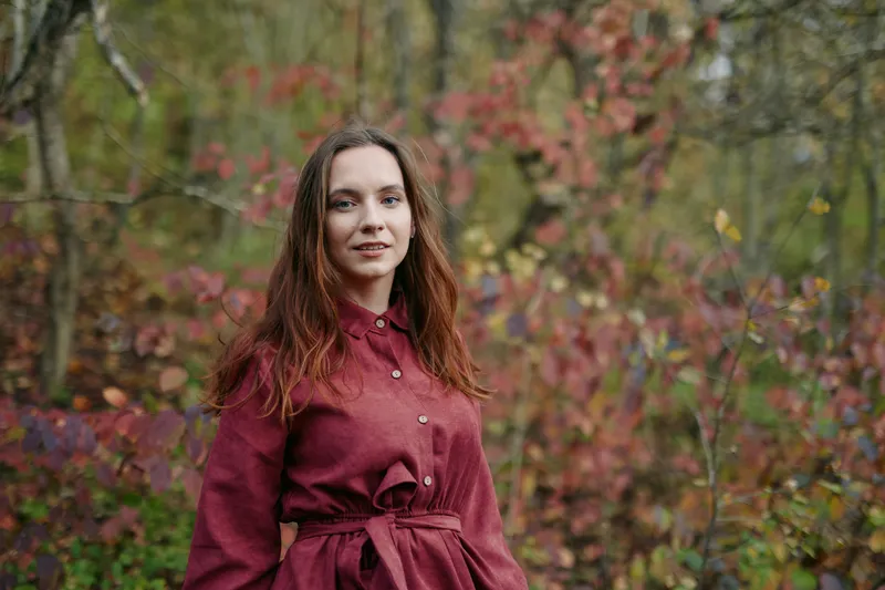 Natural portrait of a young woman in autumn foliage, conveying genuine emotion and understated style with a focus on authentic presence and credible, unposed storytelling.