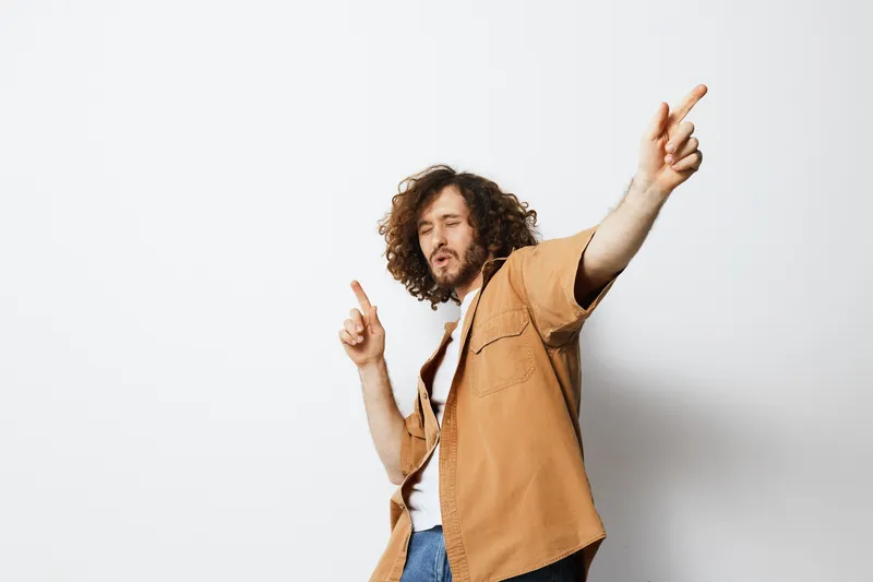 Young man with curly hair dancing joyfully in a casual outfit against a minimalist background, conveying a mood of happiness and freedom