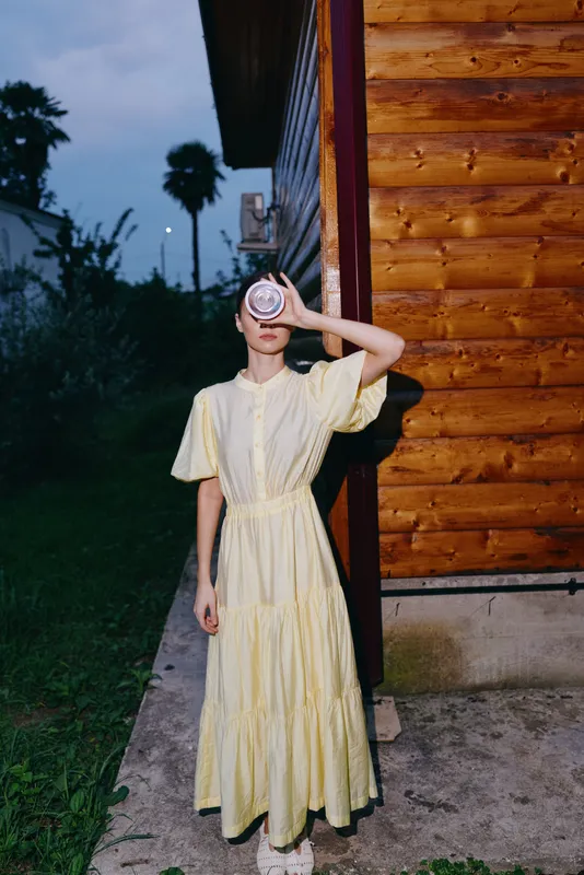 woman in yellow vintage dress portrait wooden house evening holding cup to face authenticity inclusivity
