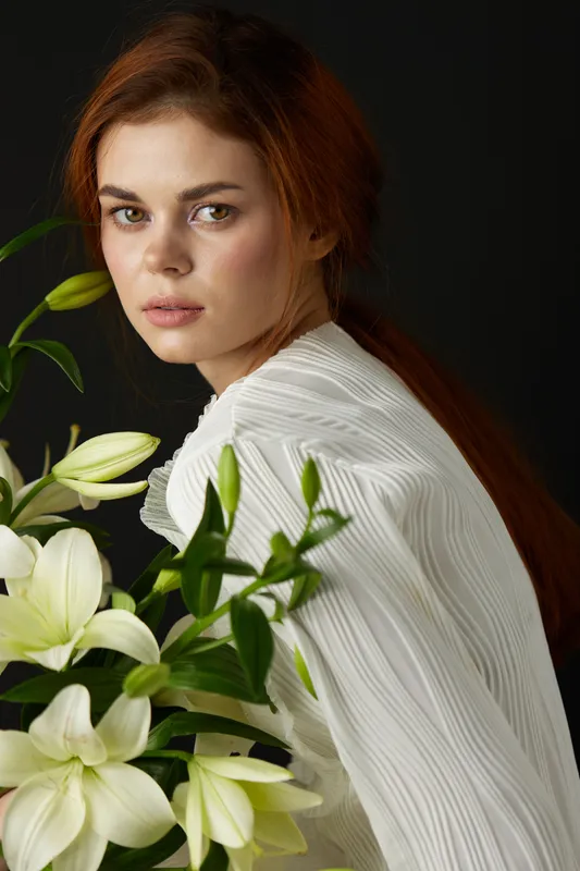 Young woman in a white blouse surrounded by white flowers, conveying a sense of serenity and elegance, ideal for concepts related to wellness, beauty, and nature