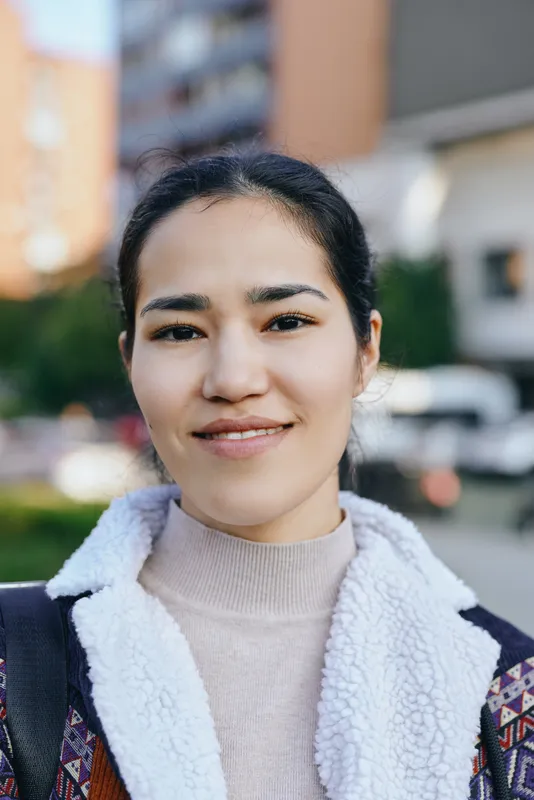 Woman with a warm smile outdoors in casual fashion wear, facing the camera in daylight on a street setting, conveying friendly, confident lifestyle vibes