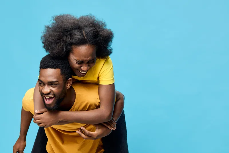 Happy cheerful couple enjoying time together against a vibrant blue background, displaying joy and connection through playful interaction in casual yellow and orange attire