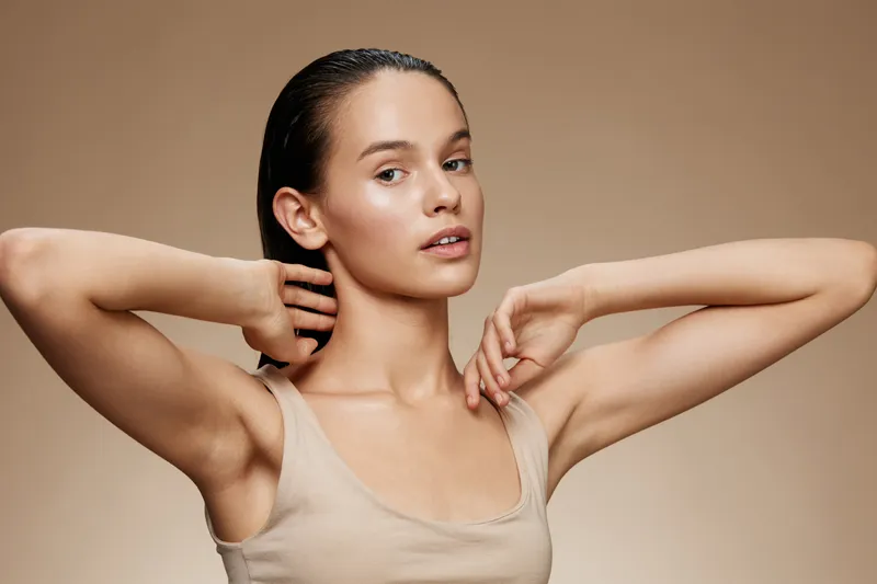 Portrait of a young woman with a neutral expression, showcasing healthy skin and natural beauty, on a soft beige background emphasizing minimalism and elegance