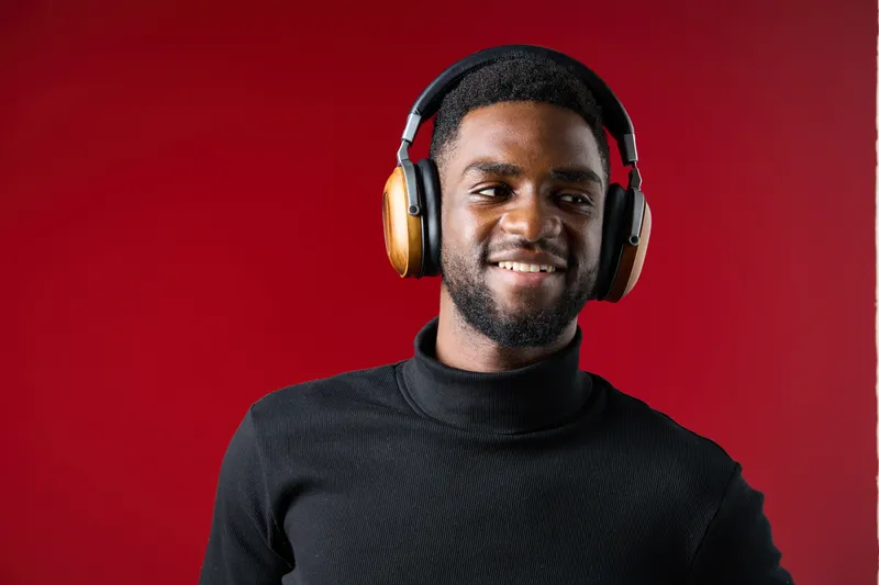 Smiling African American man in stylish headphones against a vibrant red background, showcasing modern fashion and cheerful emotions while enjoying music