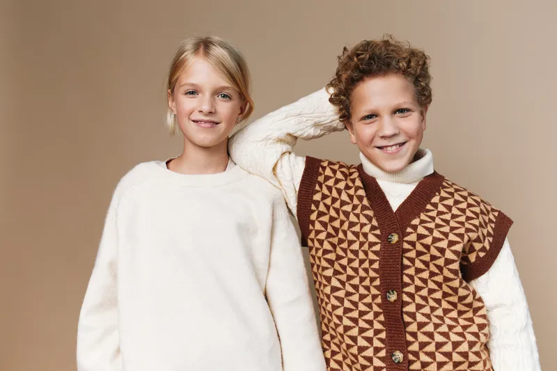 Two smiling children pose together in cozy sweaters, showcasing warm casual style and comfort against a soft neutral backdrop. Perfect for lifestyle and family themed projects.
