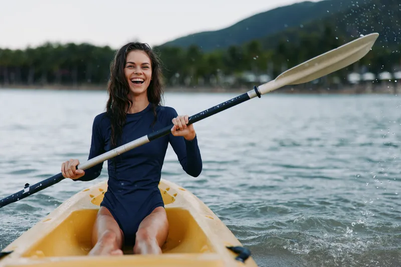 Smiling woman kayaking on lake with paddle in summer, enjoying outdoor adventure, active lifestyle, water sport, nature background.