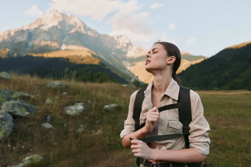 Young woman with brunette hair enjoys a peaceful moment hiking in the mountains during golden hour with a relaxed expression and casual outdoor clothing.