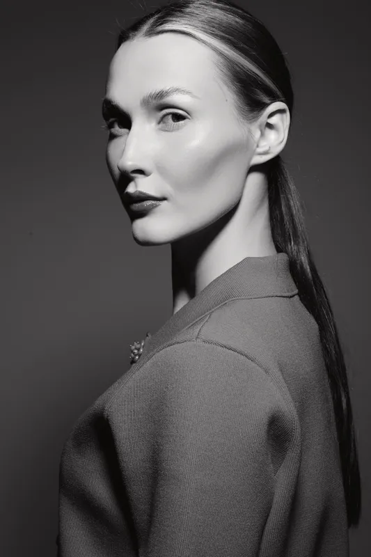 Portrait of a young Caucasian woman with fair skin and slicked back hair wearing a textured jacket against dark background. Concept of elegance and style.