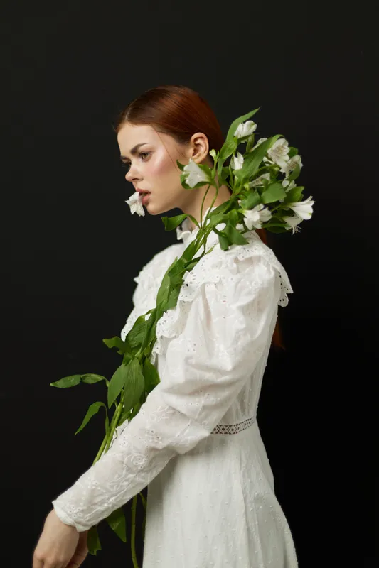 Young woman in a white dress holding greenery, expressing calmness and elegance against a dark background, ideal for wellness or fashion themes