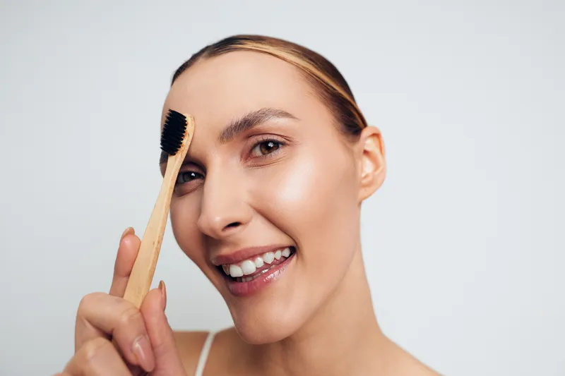 Smiling woman holding hair brush for grooming beauty care routine, close up, natural light, smooth skin, relaxed expression, clean white background, soft breeze