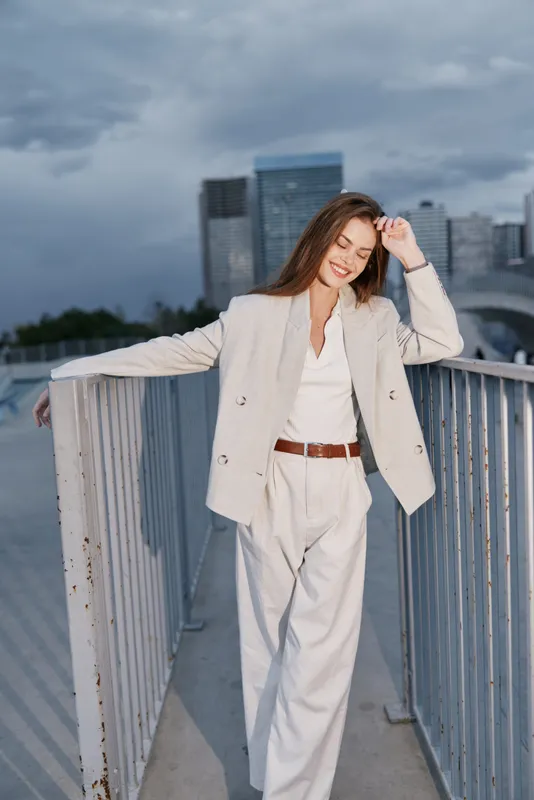 Confident woman in business attire smiling outdoors against an urban skyline, showcasing professionalism and elegance in a sleek, modern environment.