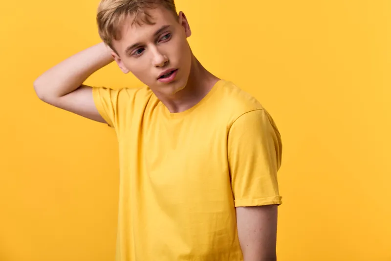 Confused man in a yellow shirt against a bright yellow backdrop, expressing hesitation and curiosity, casual fashion, modern mood for studio lifestyle imagery
