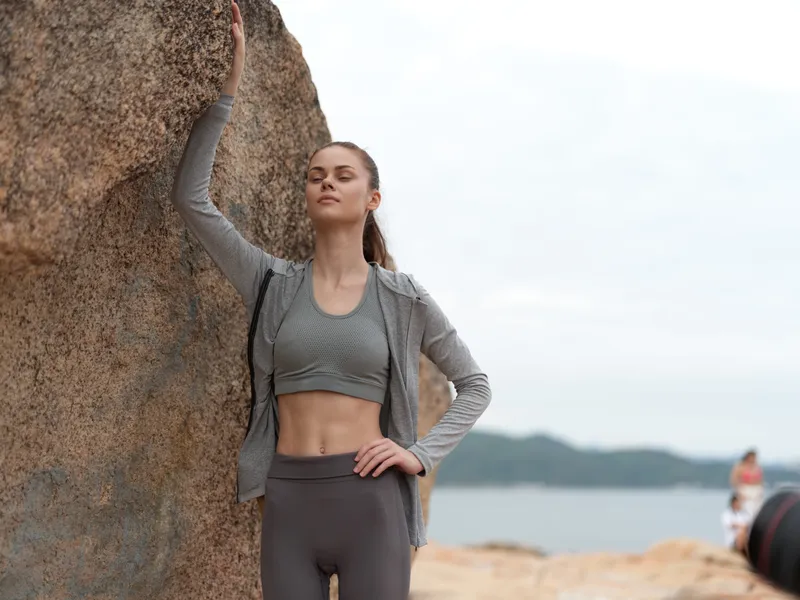 Young athletic woman in sporty attire posing confidently outdoors, showcasing fitness and empowerment against a natural rocky backdrop
