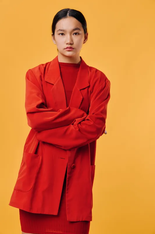 Young woman wearing red jacket and sweater standing with crossed arms on yellow background. Serious expression with confident posture and casual fashion style in studio.