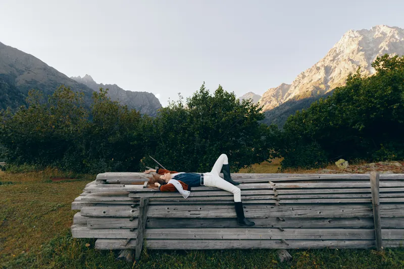 woman mountains bench meadow nature relaxing outdoors forest scene with a person lying on a wooden fence in a peaceful countryside setting, sunlight and scenic alpine landscape