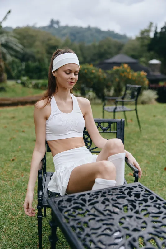 Young athletic woman enjoying a moment of relaxation in activewear, seated outdoors in a serene garden setting, showcasing a healthy lifestyle and natural beauty