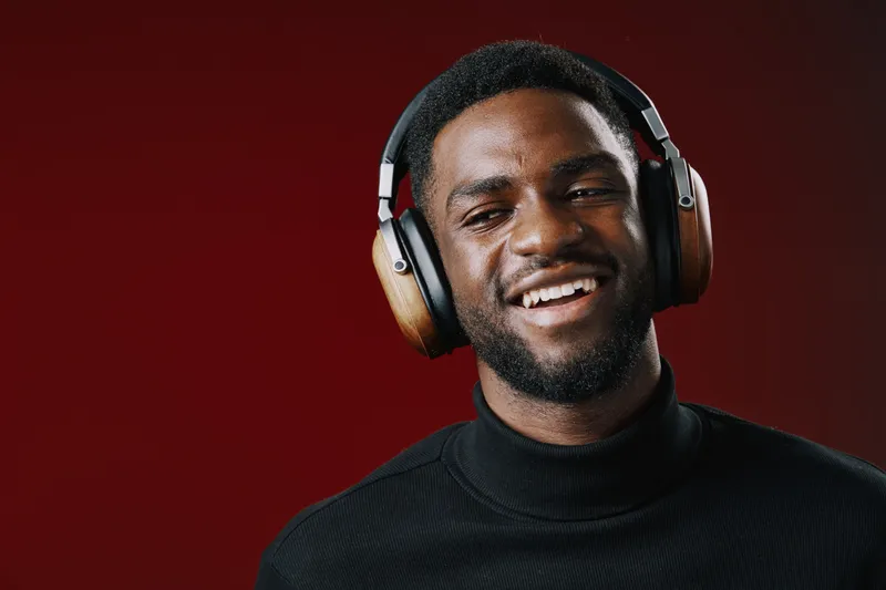 Happy young Black man smiling while wearing headphones against a vivid red background, embodying the joy of music and personal connection